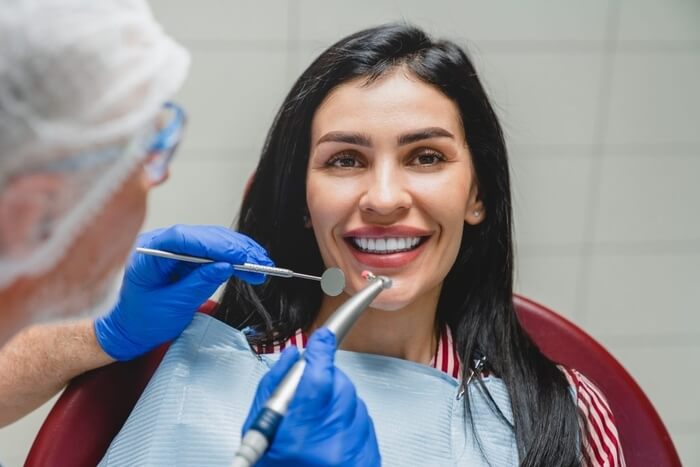 Ideal perfect smile. Caucasian beautiful woman smiling while dentist orthodontist applying veneers, whitening her teeth, filling tooth, curing caries decay. Stomatology concept